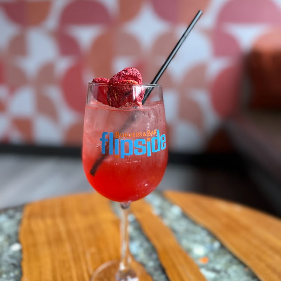 A red cocktail with dried strawberries and a black straw in a Flipside branded glass.