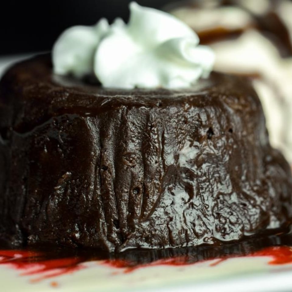 A dark chocolate lava cake topped with whipped cream, drizzled with raspberry sauce and ice cream.