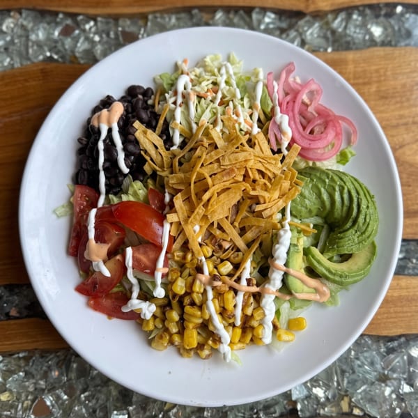 Colorful salad with black beans, corn, avocado, tomatoes, pickled onions, tortilla strips, and dressings.