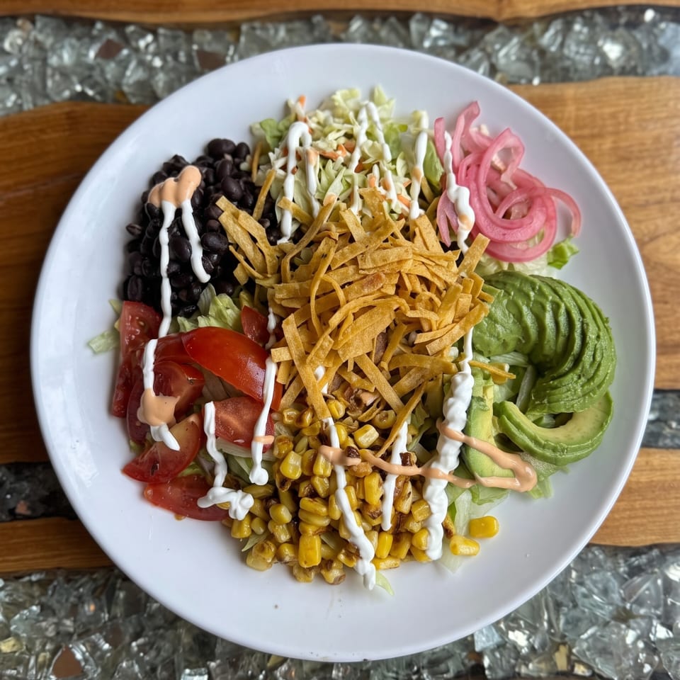 Colorful salad with black beans, corn, avocado, tomatoes, pickled onions, tortilla strips, and dressings.
