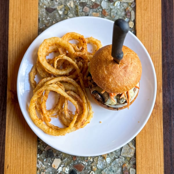 Gourmet burger with mushrooms and pickled carrots, skewered with a knife, served with crispy onion rings.