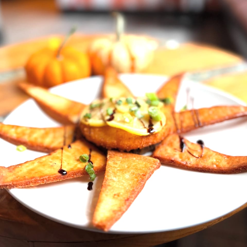 Star-shaped fried appetizer with central fritter, yellow squash, green onions, and balsamic glaze.