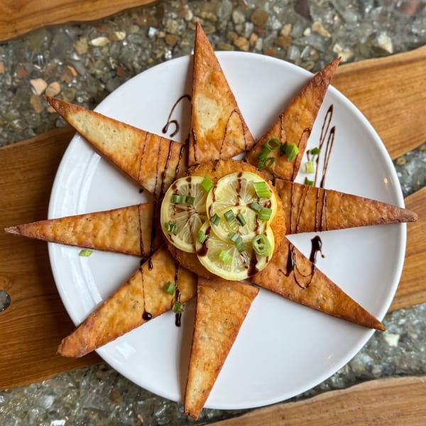 Star-shaped fried appetizer with lemon, green onions, and balsamic glaze on a white plate.