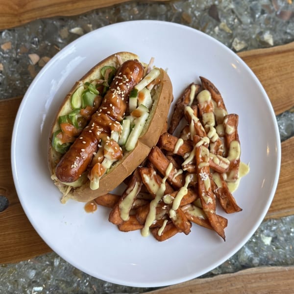 Hot dog with sesame seeds, cucumber, and sauce, served with sweet potato fries.